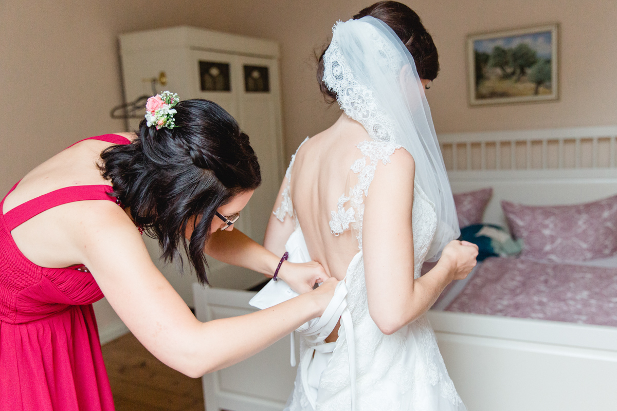 Die Trauzeugin hilft der Braut ins Brautkleid.
